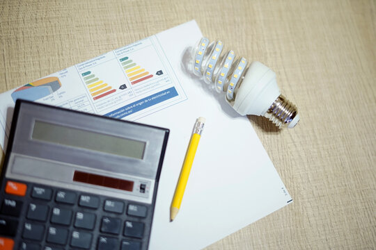 Bombilla de bajo consumo LED junto con facturas de luz, un lapicero y calculadora. El foco en la bombilla.