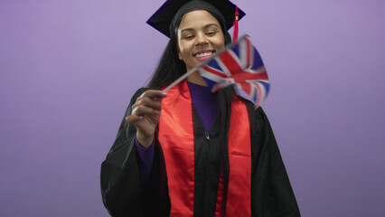 Woman waves uk flag in purple studio wearing graduation gown; academic achievement celebration...