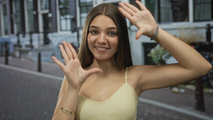 Caucasian teenage girl smiling holds hands framing cobblestone urban street scene; imagination creativity joy.