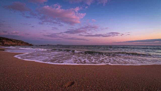 A serene beach scene during sunset with gentle waves and a colorful sky.