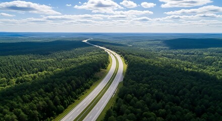 Expansive highway cutting through a lush green forest under a cloudy blue sky