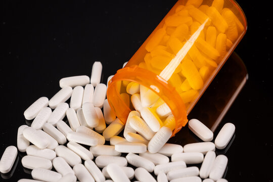 Tylenol/Acetaminophen Editorial: Pills spilling out of an orange pill bottle onto a balck surface.