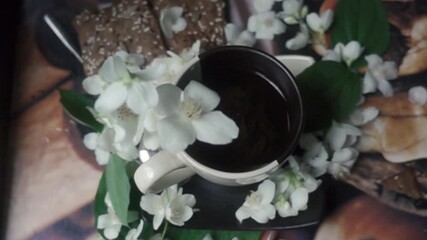 A delicate jasmine flower gently falls into a cup of warm tea, surrounded by fragrant blossoms and light snacks. A serene moment of tranquility.