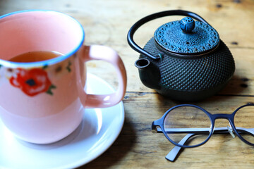 tomando el té de una tetera de hierro negra con una taza rosa en una mesa de madera vieja  con...