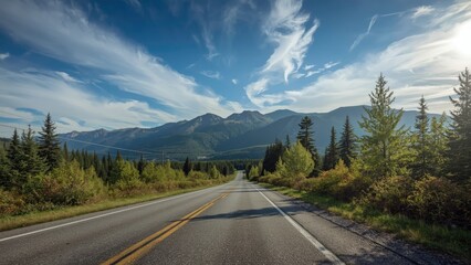 Naklejka premium A scenic mountain road surrounded by trees under a blue sky with clouds. Nature and landscape, travel and adventure, outdoor scenery. The concept of road trip and exploring nature.