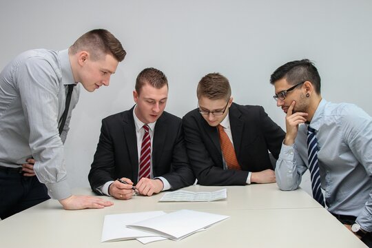 Collaborative Startup Team Meeting in Modern Office Workspace. A group of young professionals collaborating inside a modern open-plan tech office. Team members are seated around computers discussing.