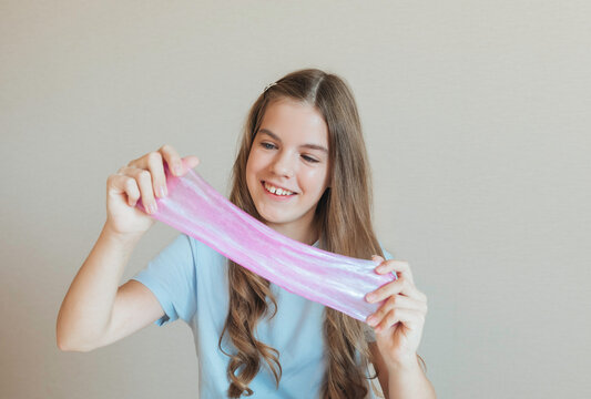Smiling girl holding and stretching shiny pink marbled slime towards the camera. Fun sensory game and creative hobby