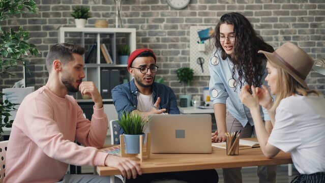 Collaborative Startup Team Meeting in Modern Office Workspace. A group of young professionals collaborating inside a modern open-plan tech office. Team members are seated around computers discussing. - Powered by Adobe