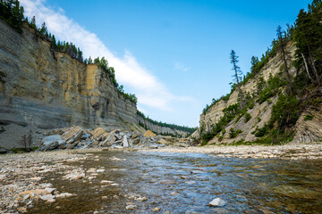 Steep Canyon, Stone Cliffs, Shallow River, Fallen Boulders, and Boreal Forest Under a Blue Sky near to Vaureal Waterfall on a Sunny Day in Anticosti, Quebec, Canda