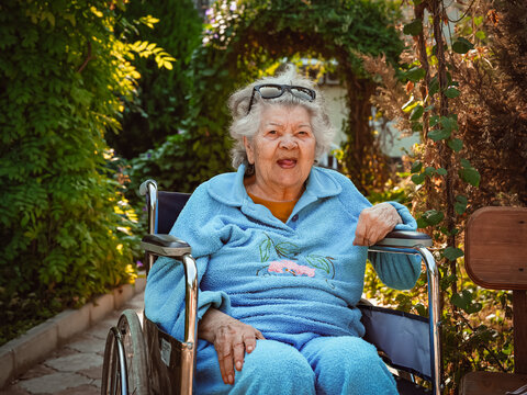 Demencia - Smiling Elderly Woman Sitting In Wheelchair: Warm Outdoor Portrait With Sunlit Garden Background And Joyful Expression