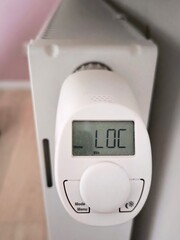A digital thermostat on a white radiator with a LOC and day of the week indicator. Close-up