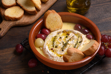 Baked camembert or brie cheese with honey, grapes, aromatic herbs and crusty bread