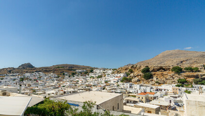 Panoramic view of white Mediterranean hillside town under clear blue summer sky, traditional houses clustered between rocky mountains, scenic travel destination.