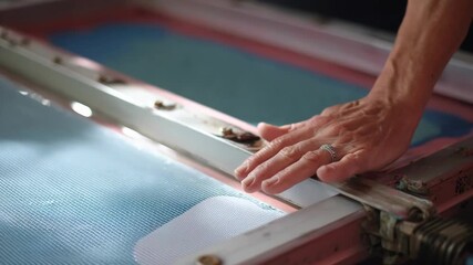 Medium shot of screen printing mesh preparation focusing on securing a tensioned frame for vibrant marketing signage production.