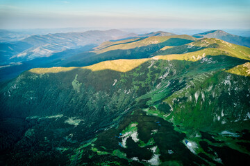 Fototapeta premium Aerial view of rugged mountain range with lush green slopes at sunset. Landscape showcases beauty of untouched nature with distant peaks and valleys bathed in soft sunlight. Carpathians, Chornogora.