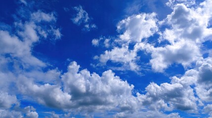 Obraz premium Fluffy white clouds drift peacefully across a vibrant blue sky in the afternoon. The scene evokes calmness and natural beauty perfect for relaxation and daydreaming.