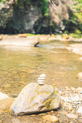 Zen stone tower balanced on large river rock against blurred water background