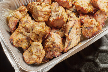 Close-up of grilled shashlik kebab pieces in a foil tray