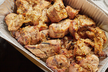 Close-up of grilled shashlik kebab pieces in a foil tray