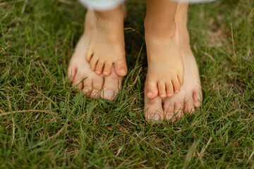Close-up of small bare feet standing on top of adult feet on green grass outdoors.