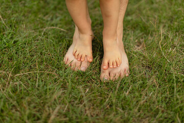 Close-up of small bare feet standing on top of adult feet on green grass outdoors.