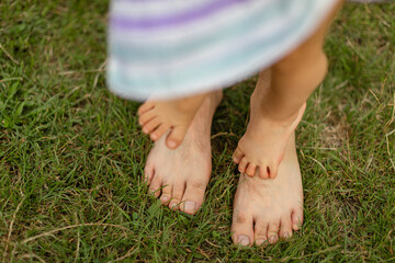 Close-up of small bare feet standing on top of adult feet on green grass outdoors.