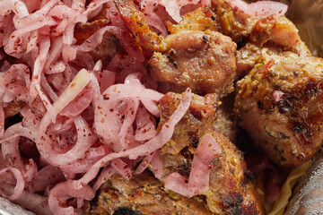 Close-up of grilled shashlik kebab pieces with marinated onions in a foil tray