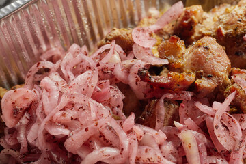 Close-up of grilled shashlik kebab pieces with marinated onions in a foil tray
