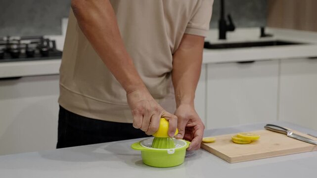 Mid-shot of hands squeezing halved lemon on manual citrus juicer. Perfect for illustrating homemade juices, wellness routines, natural detox drinks, and kitchen preparations.