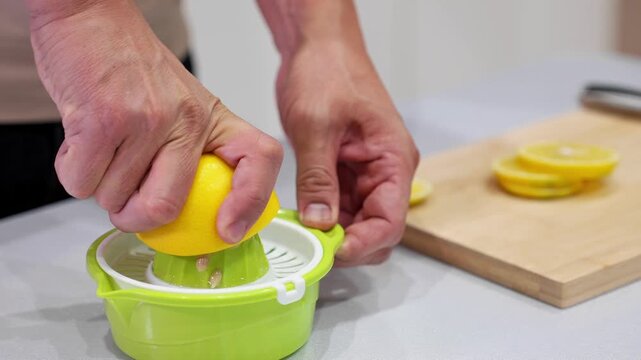 Macro view of hands squeezing lemon on manual juicer with visible juice and seeds. Ideal for food blogs, detox themes, citrus beverage preparation, and fresh ingredient visuals.