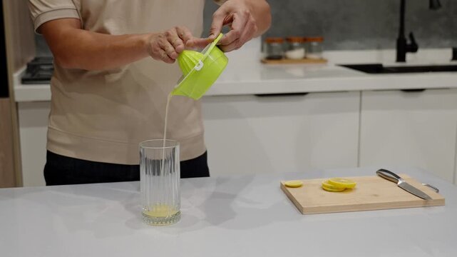Male person pouring fresh lemon juice from manual juicer into tall glass. Suitable for healthy drink recipes, detox concepts, morning wellness routines, and natural beverage themes.