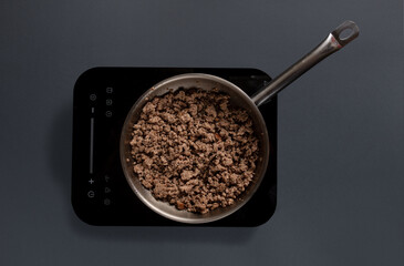 Ground meat browns in a stainless-steel pan on an electric stove. The kitchen setting is simple, focusing on the cooking process of the meat preparation.