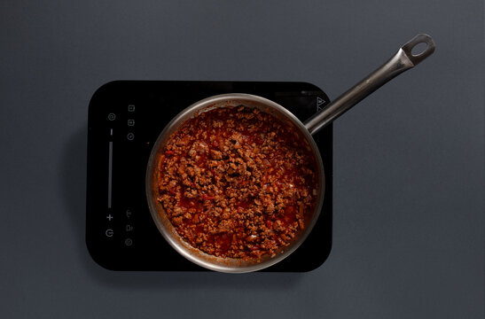 A pot filled with a rich meat sauce is simmering on an electric stove. The sauce contains ground meat, tomatoes, and spices, showcasing a cozy cooking moment in a contemporary kitchen.