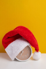 Alarm clock covered with santa hat on color background. Holiday Countdown
