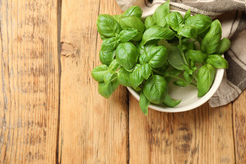 Fresh basil leaves in bowl on wooden table, top view. Space for text