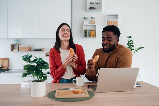 Happy diverse couple enjoying croissant breakfast at home