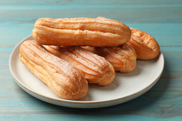 Tasty eclairs with powdered sugar on turquoise wooden table, closeup