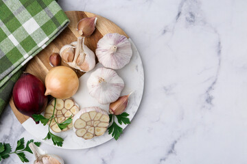 Garlic, onions, and parsley on white marble table, flat lay. Space for text