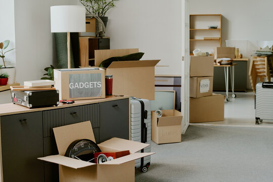 Cardboard boxes labeled with various items scattered in modern apartment, suitcases and packed belongings indicating young couple moving and preparing for home renovations