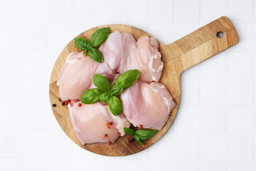 Raw chicken thighs with basil and peppercorns on white tiled table, top view