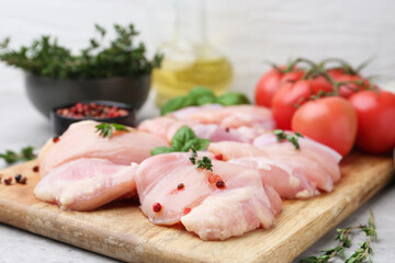 Raw chicken thighs with herbs, peppercorns and tomatoes on light table, closeup
