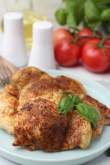 Tasty roasted chicken thighs with basil served on white tiled table, closeup