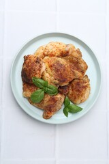 Tasty roasted chicken thighs with basil on white tiled table, top view