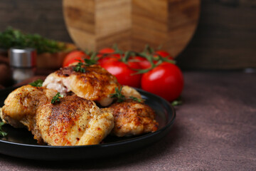 Tasty cooked chicken thighs with thyme and tomatoes on brown table, closeup. Space for text