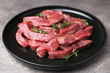 Pieces of raw beef meat and thyme on grey table, closeup