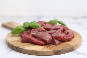 Pieces of raw beef meat and basil on white marble table, closeup