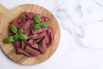 Pieces of raw beef meat and basil on white marble table, top view. Space for text