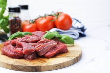 Pieces of raw beef meat, basil and ingredients on white marble table, closeup. Space for text