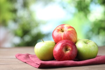 Fresh red and green apples on wooden table against blurred green background, closeup. Space for text