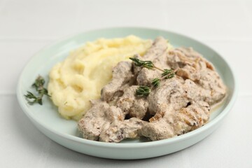 Delicious beef stroganoff with mashed potatoes and thyme on white tiled table, closeup